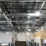 Exposed ductwork, wiring, and metal ceiling inside a Sierra Trading Commercial HVAC Spokane Valley project, with a ladder and construction materials visible below.