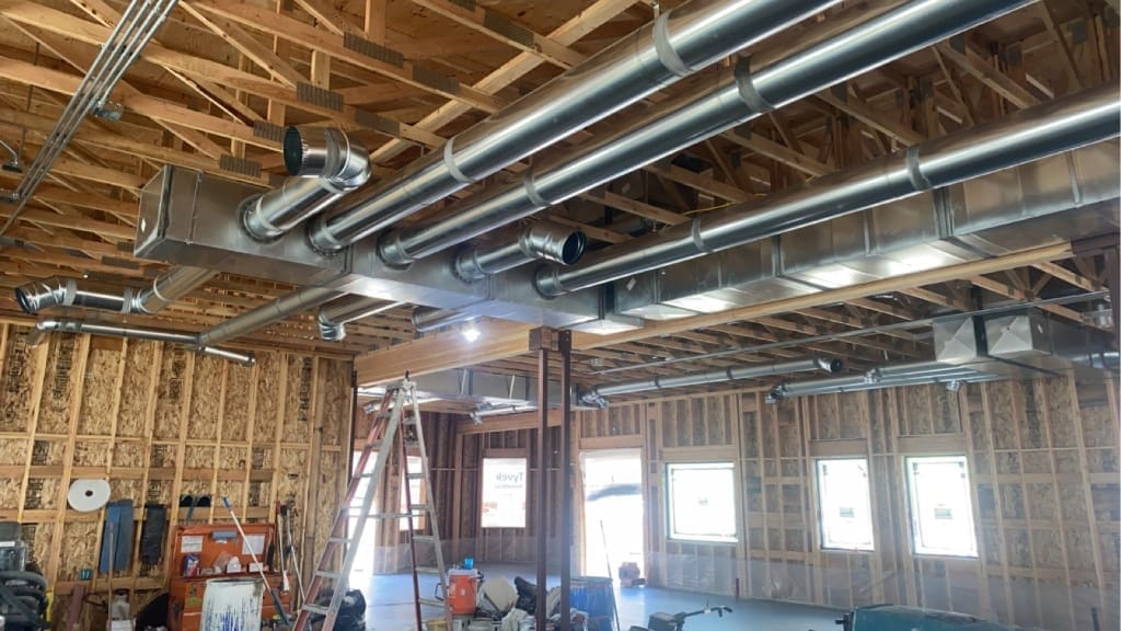 Large metal Commercial HVAC ducts installed on the ceiling of a building under construction, featuring exposed wooden framing and windows along one wall—perfect for new construction projects.
